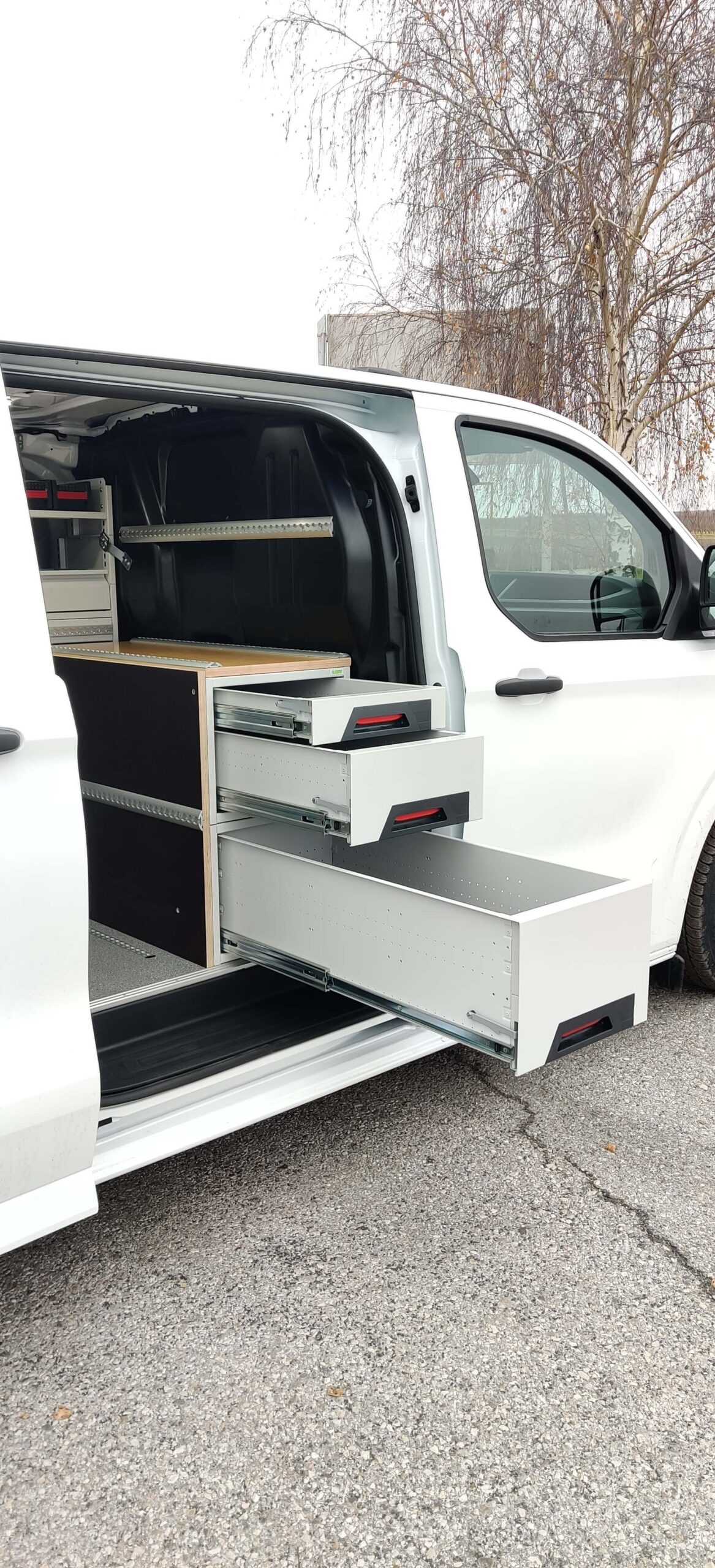 Modulare Fahrzeugeinrichtung mit offenen Schubladen in einem weißen Transporter, ideal für effiziente Ladungssicherung.